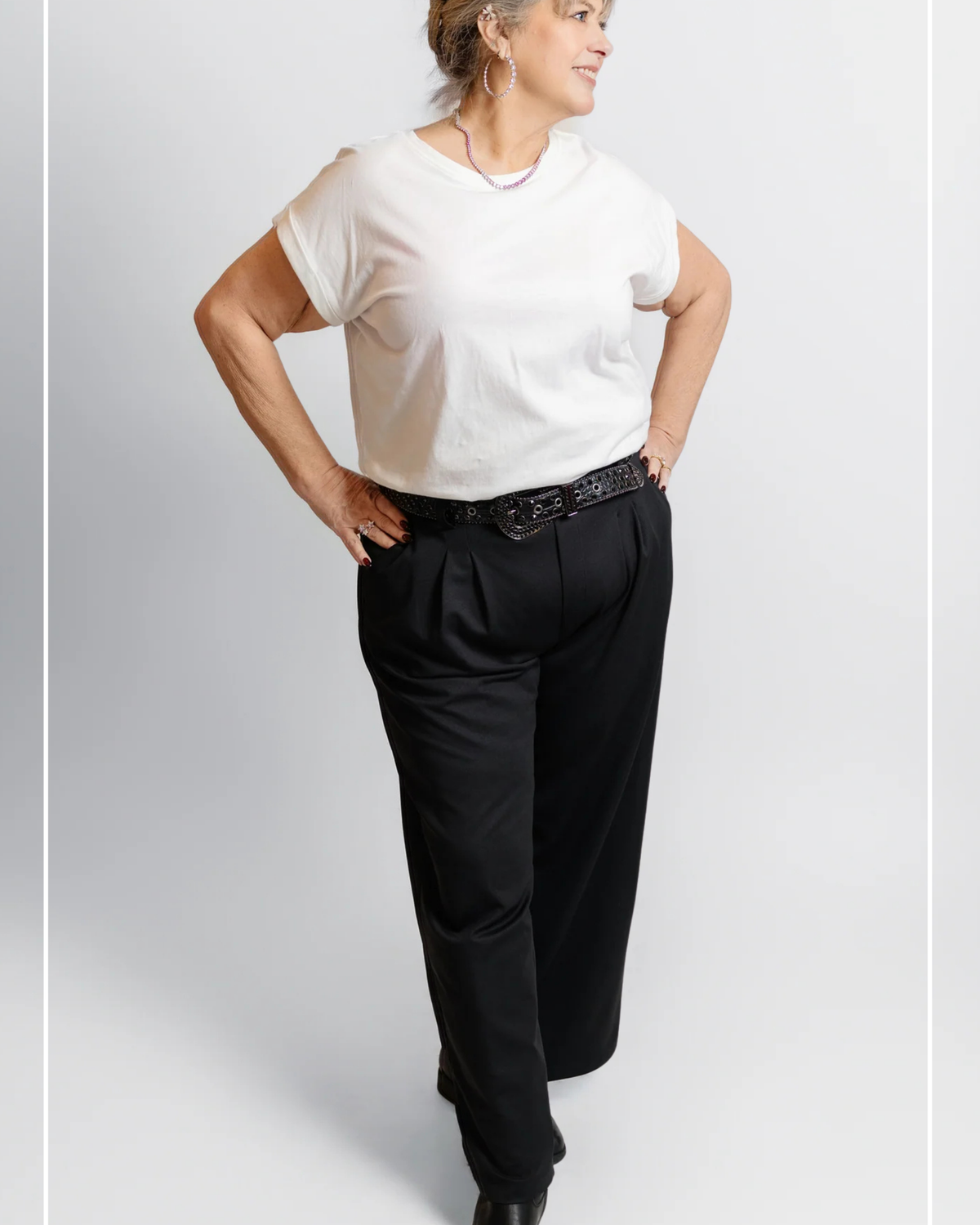Person wearing a white t-shirt and black pants on a plain background | Model Photo - Trisha | Harlow + James Boutique | West Des Moines, IA
