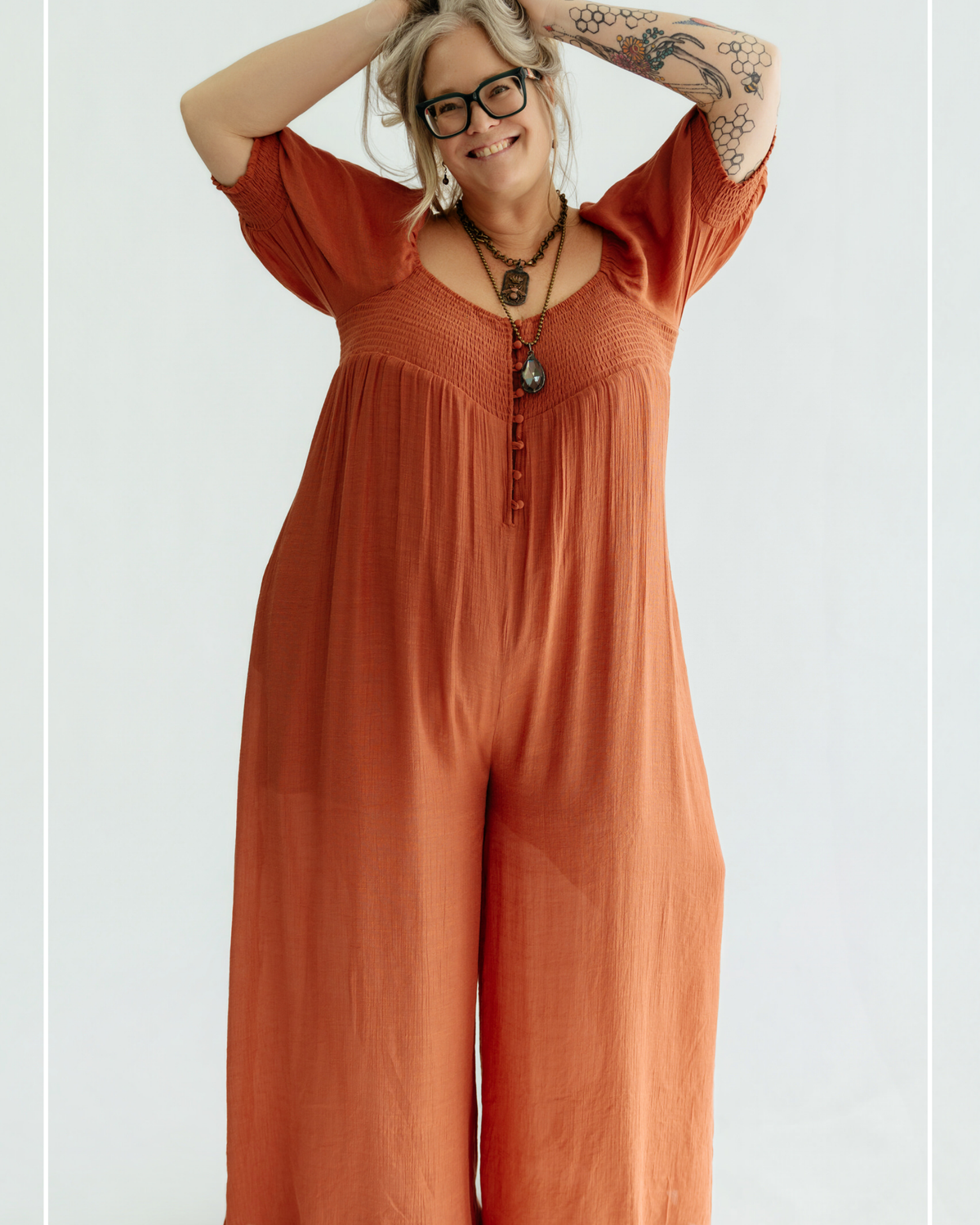 Woman wearing a rust-colored jumpsuit with a plain background | Model Photo - Shannon | Harlow + James Boutique | West Des Moines, IA