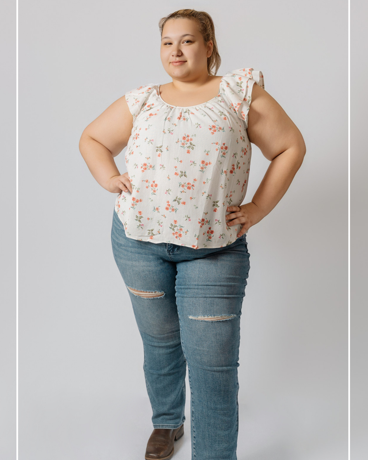 Woman wearing a floral blouse and ripped jeans on a plain background | Model Photo - Lauryn | Harlow + James Boutique | West Des Moines, IA