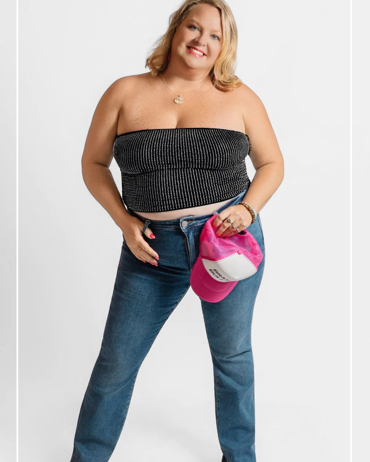 Woman wearing a black strapless top and blue jeans with a pink bag on a white background | Model Photo - Staci | Harlow + James Boutique | West Des Moines, IA