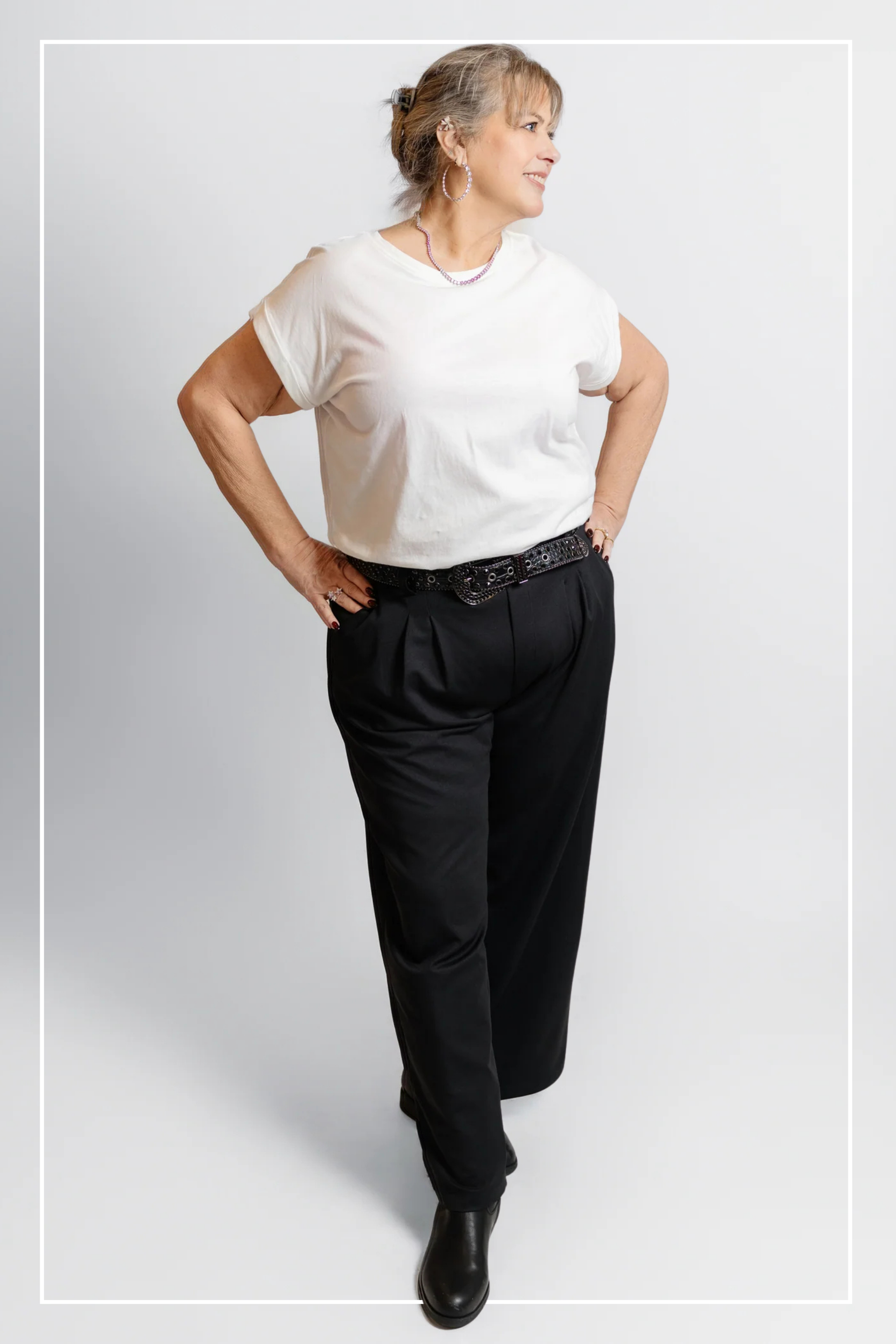 Person wearing a white t-shirt and black pants on a plain background | Model Photo - Trisha | Harlow + James Boutique | West Des Moines, IA