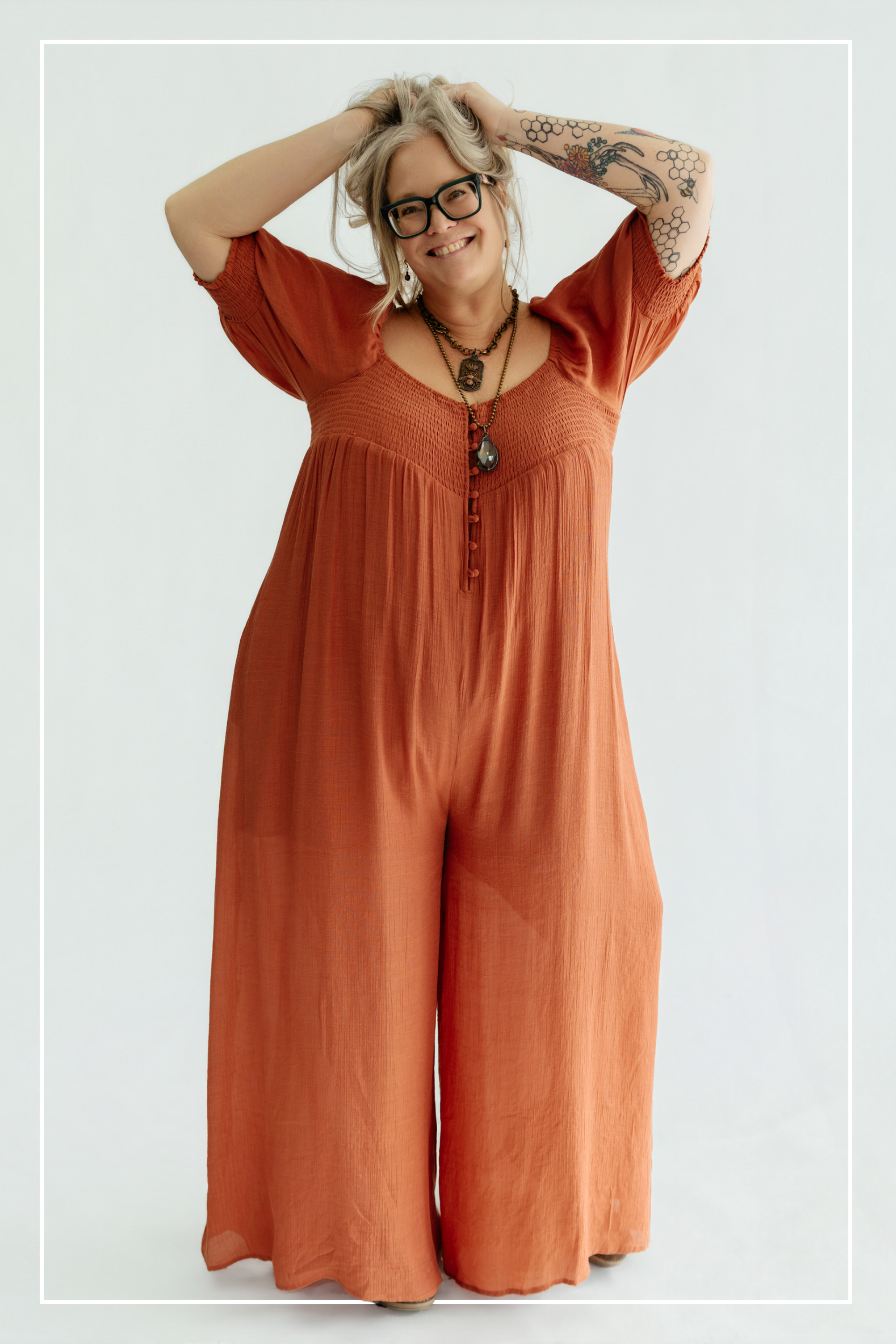 Woman wearing a rust-colored jumpsuit with a plain background | Model Photo - Shannon | Harlow + James Boutique | West Des Moines, IA