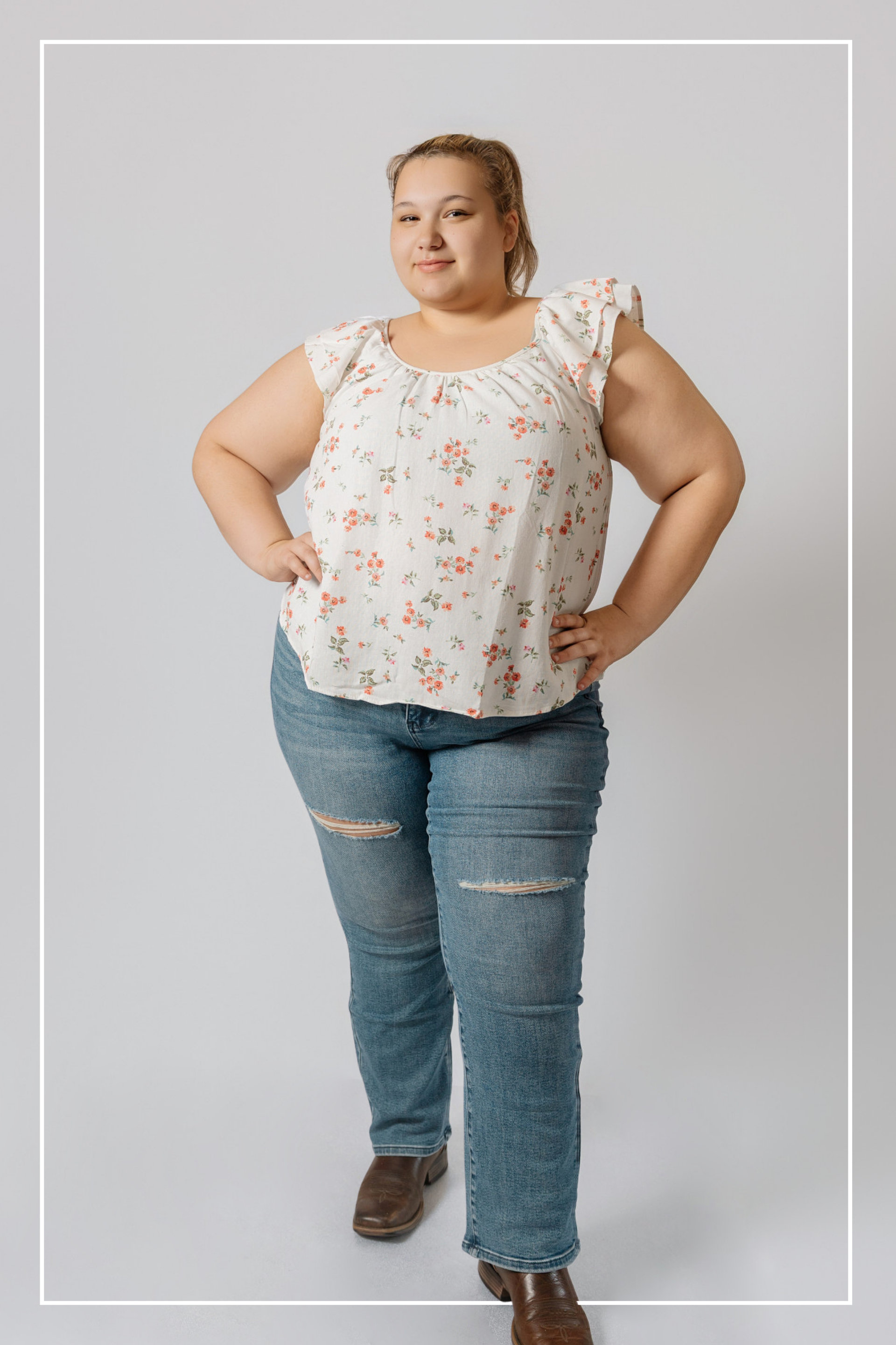 Woman wearing a floral blouse and ripped jeans on a plain background  | Model Photo - Lauryn | Harlow + James Boutique | West Des Moines, IA