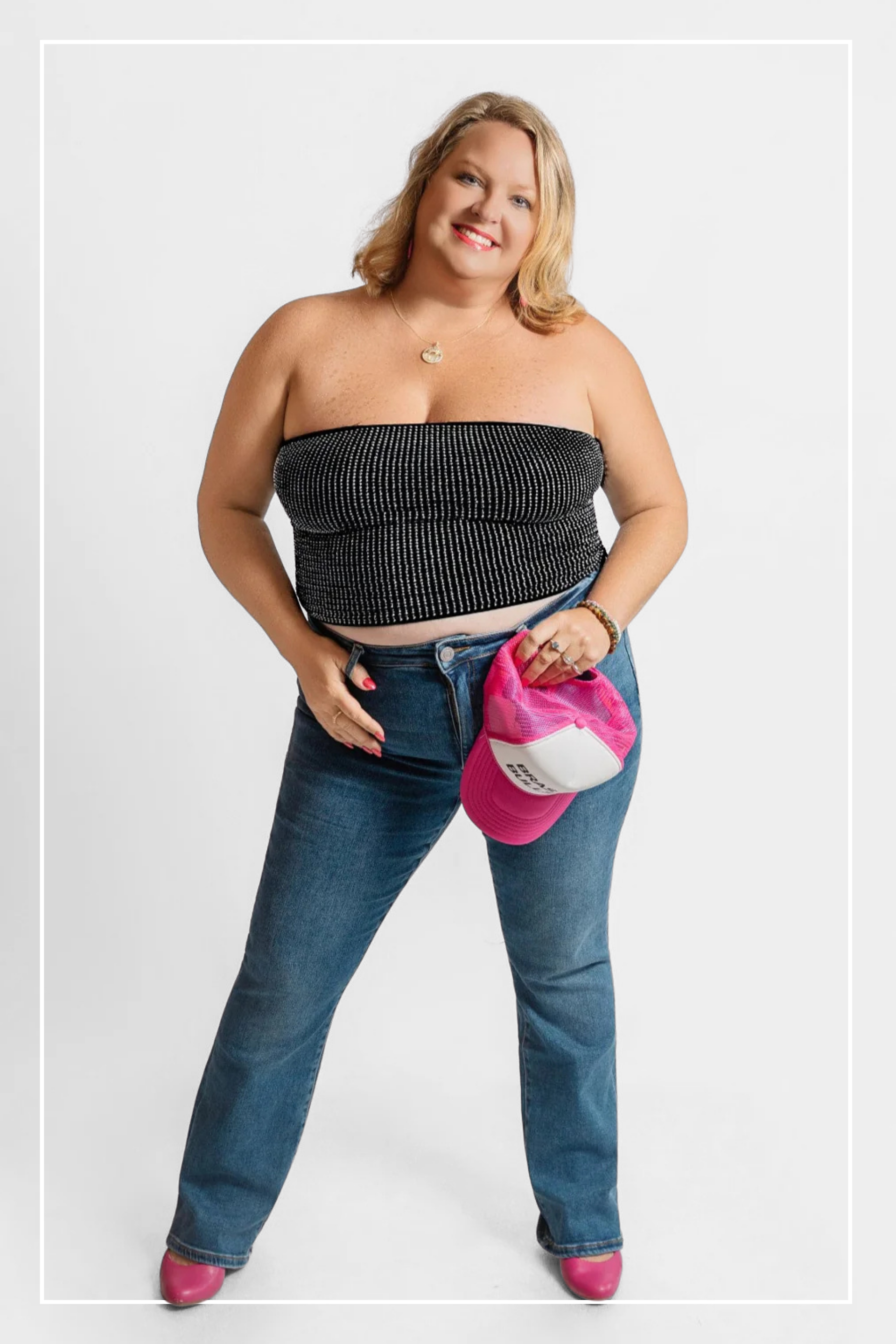 Woman wearing a black strapless top and blue jeans with a pink bag on a white background | Model Photo - Staci | Harlow + James Boutique | West Des Moines, IA