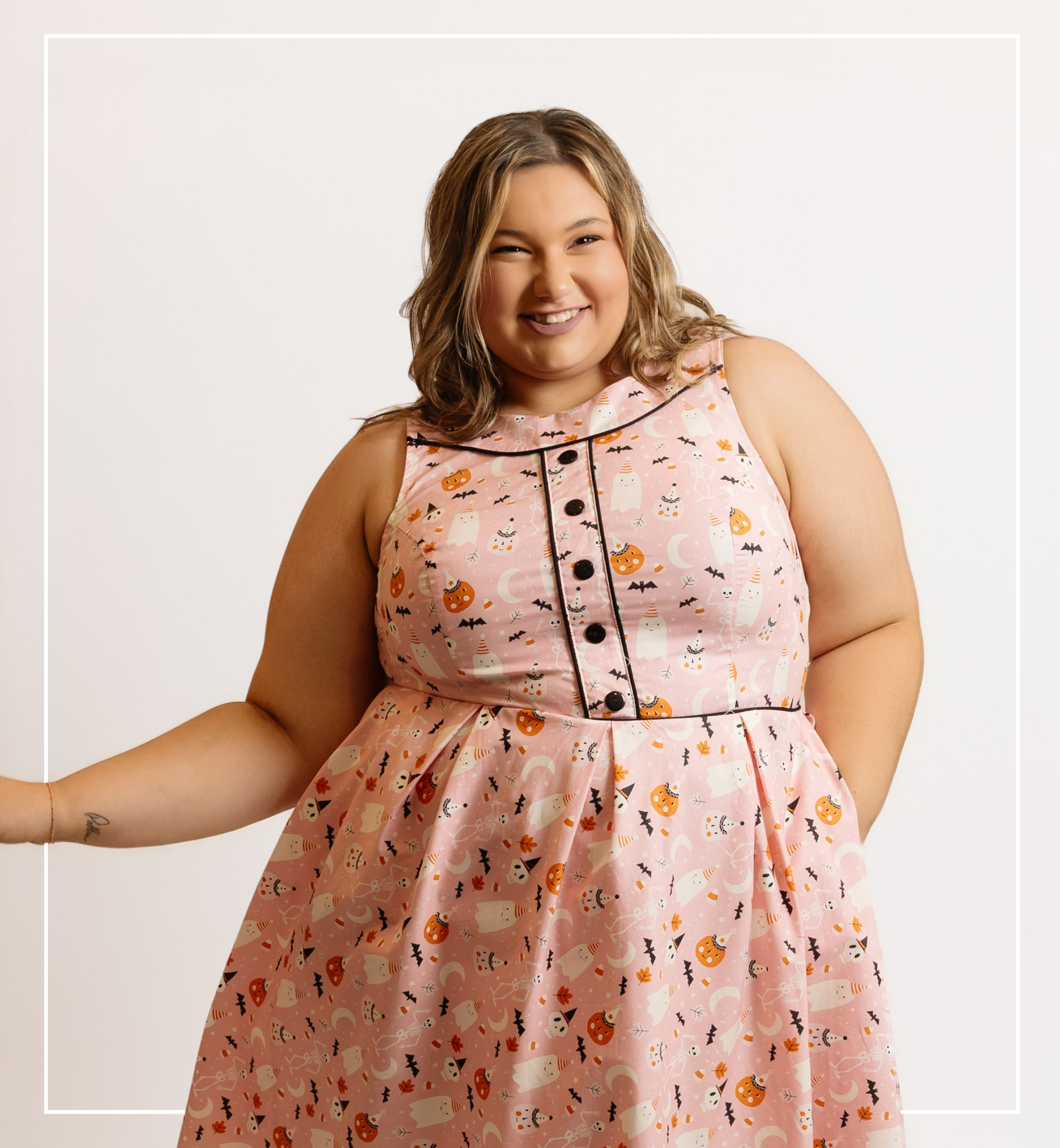 Woman wearing a pink dress with a pattern of small images on a white background | Staff - Lauryn | Harlow + James Boutique | West Des Moines, IA